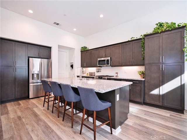 kitchen with dark brown cabinetry, a breakfast bar area, a center island with sink, light hardwood / wood-style flooring, and appliances with stainless steel finishes