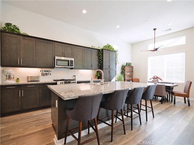 kitchen with sink, range, dark brown cabinets, an island with sink, and light wood-type flooring