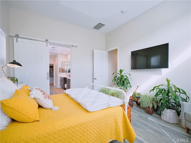 bedroom with a barn door, ensuite bath, and light hardwood / wood-style floors