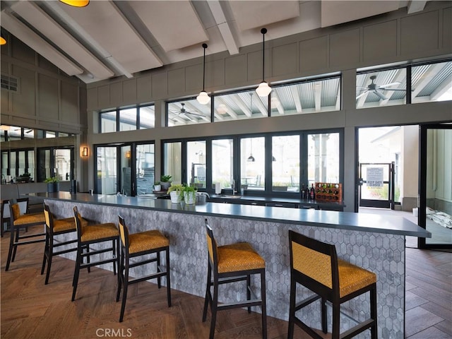 bar featuring ceiling fan, dark parquet flooring, hanging light fixtures, and vaulted ceiling with beams