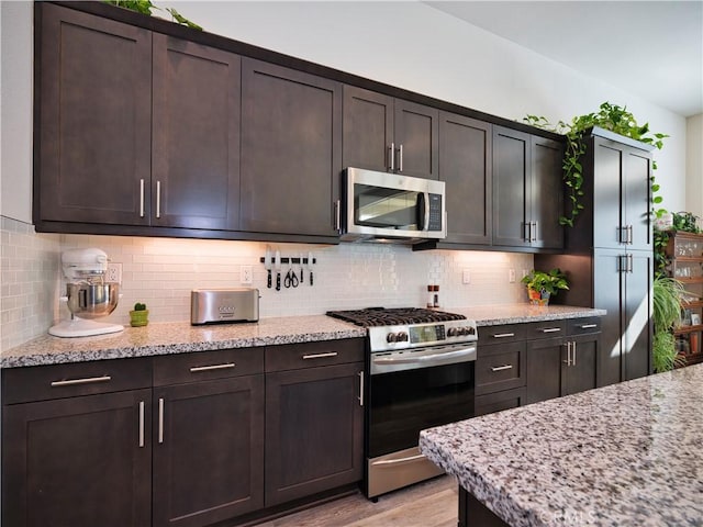 kitchen featuring appliances with stainless steel finishes, dark brown cabinets, and light stone counters
