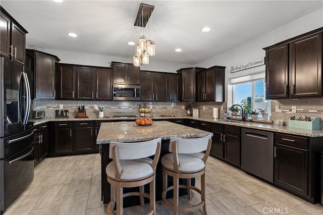 kitchen featuring appliances with stainless steel finishes, decorative light fixtures, sink, a center island, and dark brown cabinets