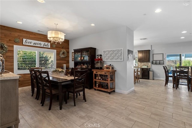 dining space featuring a notable chandelier, a wealth of natural light, and wooden walls