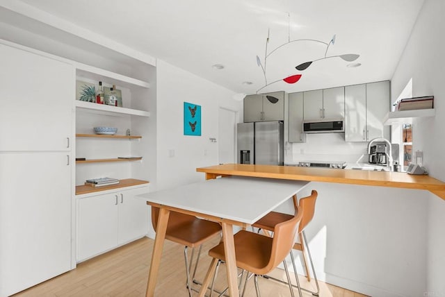 kitchen with built in shelves, gray cabinetry, appliances with stainless steel finishes, kitchen peninsula, and light hardwood / wood-style floors