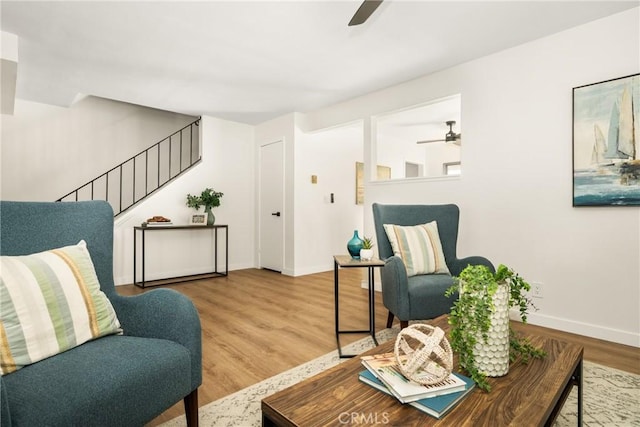 living area with baseboards, stairs, a ceiling fan, and wood finished floors