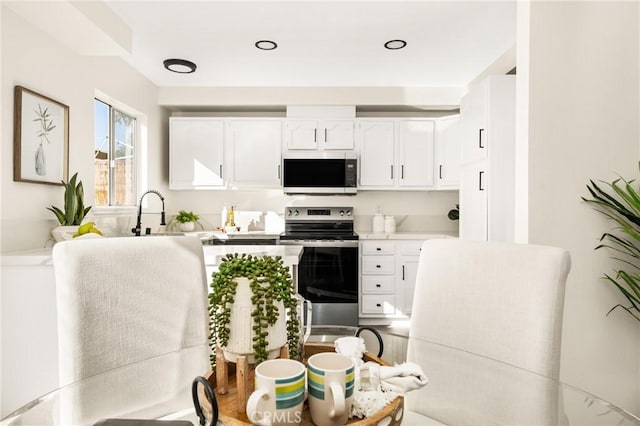 kitchen with a sink, stainless steel electric range, light countertops, and white cabinetry