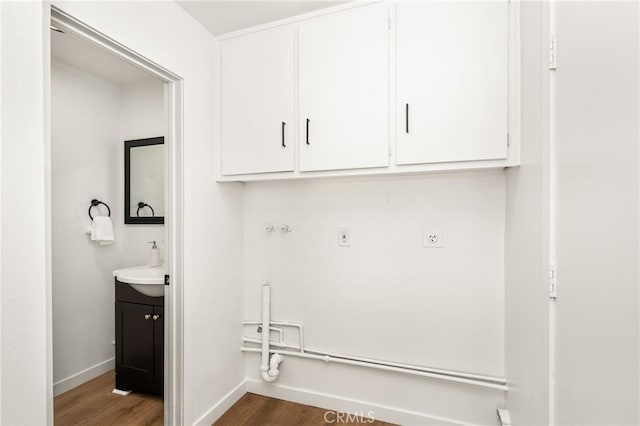 clothes washing area with cabinet space, baseboards, and wood finished floors