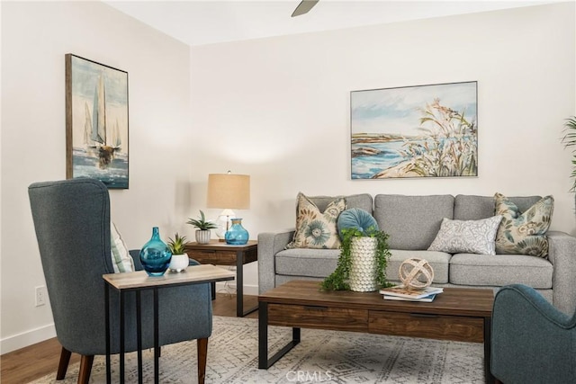 living area with a ceiling fan, wood finished floors, and baseboards