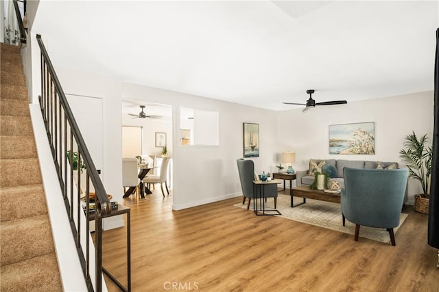 living room featuring stairs, light wood-style flooring, baseboards, and ceiling fan