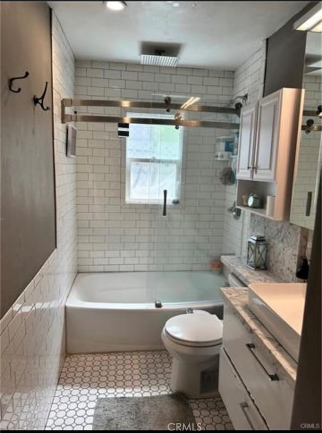 full bathroom with tiled shower / bath, tile walls, vanity, toilet, and tile patterned floors