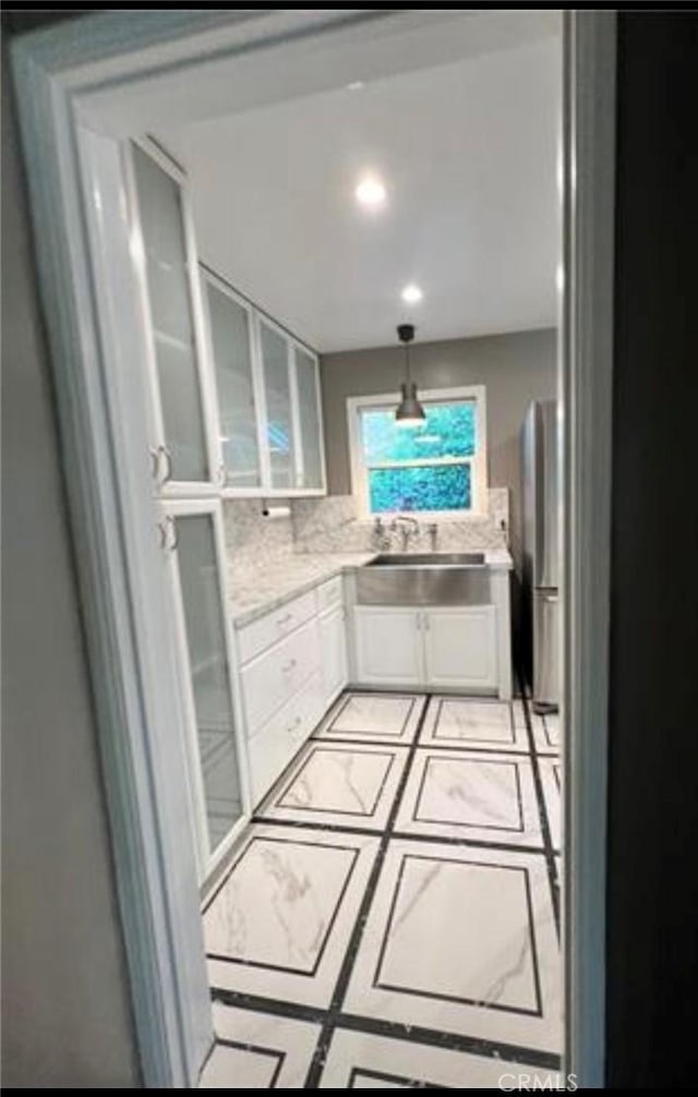 kitchen featuring decorative light fixtures, tasteful backsplash, sink, white cabinets, and light tile patterned floors