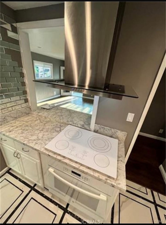 kitchen with backsplash, white appliances, light stone countertops, and island exhaust hood