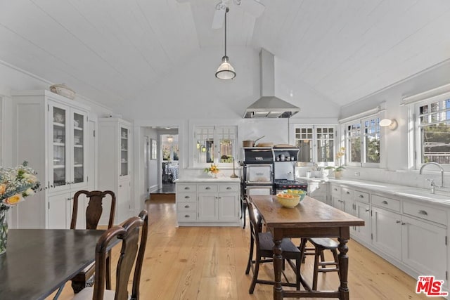 kitchen with sink, white cabinetry, hanging light fixtures, island exhaust hood, and light hardwood / wood-style floors