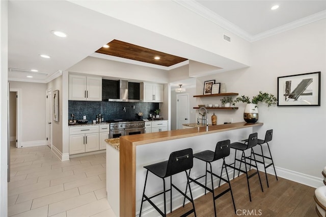 kitchen featuring white cabinetry, wall chimney range hood, kitchen peninsula, and range with two ovens