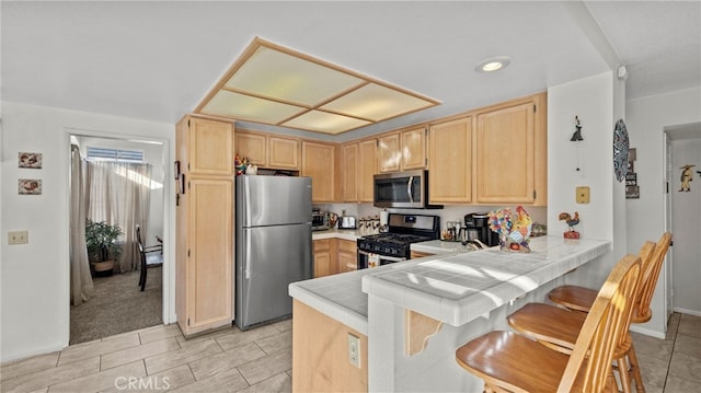 kitchen featuring appliances with stainless steel finishes, tile countertops, light brown cabinetry, and kitchen peninsula