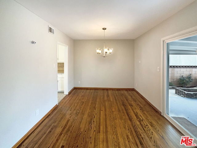 unfurnished room featuring an inviting chandelier and dark hardwood / wood-style flooring