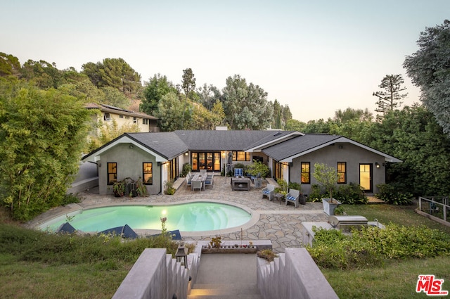 back house at dusk featuring a fenced in pool and a patio