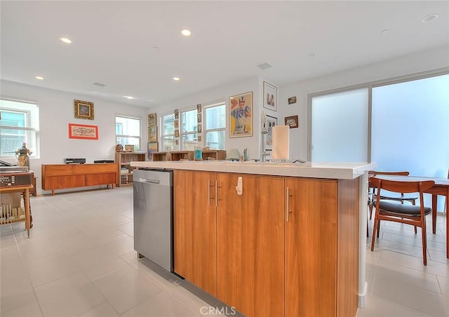 kitchen featuring light tile patterned floors, stainless steel dishwasher, and a center island with sink