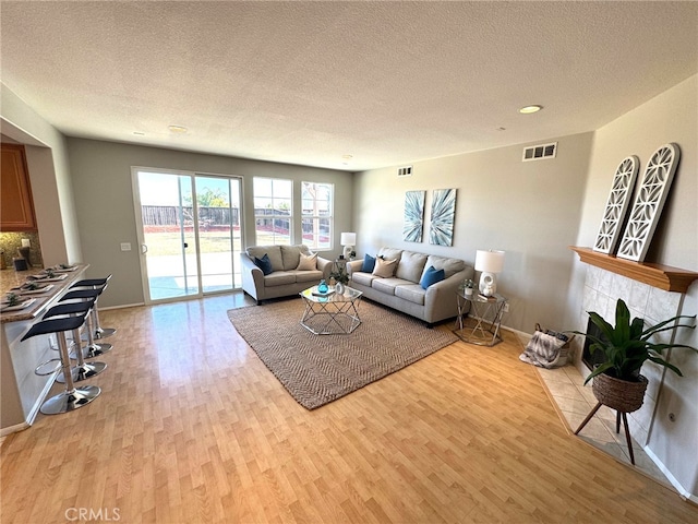 living room with a tiled fireplace, light hardwood / wood-style flooring, and a textured ceiling