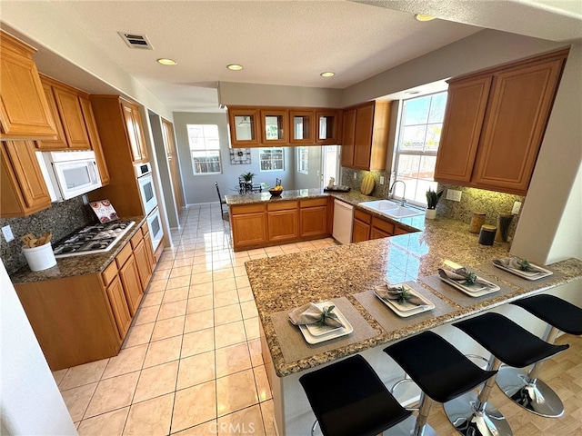 kitchen featuring light tile patterned flooring, a breakfast bar, sink, kitchen peninsula, and white appliances