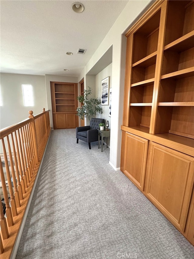 corridor featuring light colored carpet, a textured ceiling, and built in shelves