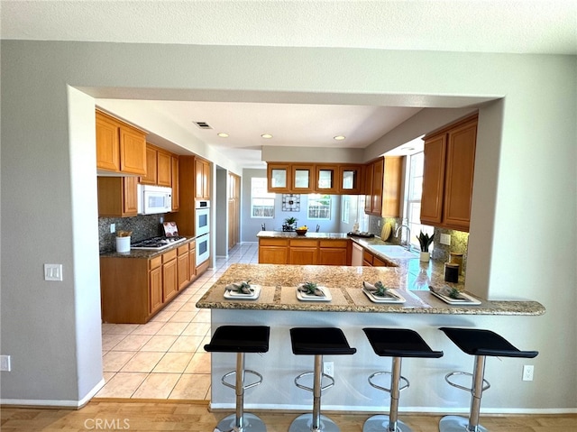 kitchen featuring white appliances, a breakfast bar area, kitchen peninsula, and decorative backsplash