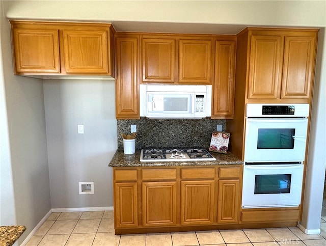 kitchen featuring light tile patterned floors, decorative backsplash, white appliances, and dark stone counters