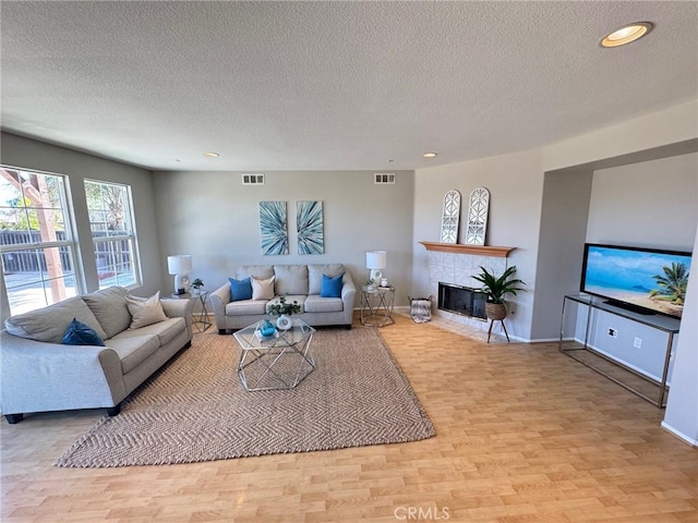 living room featuring a tiled fireplace, light hardwood / wood-style flooring, and a textured ceiling