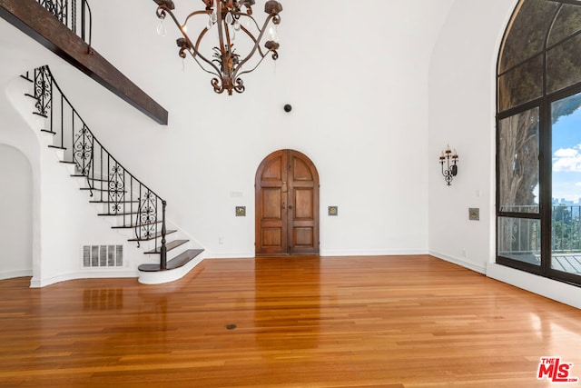 foyer entrance featuring beam ceiling, hardwood / wood-style floors, a notable chandelier, and a high ceiling