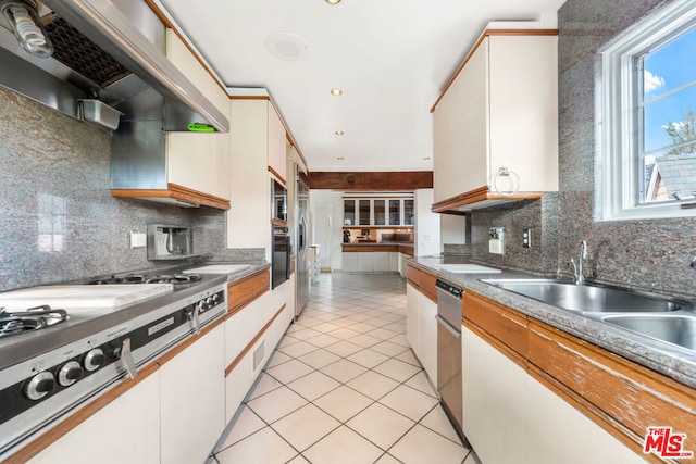 kitchen featuring tasteful backsplash, light tile patterned floors, white cabinets, and range hood