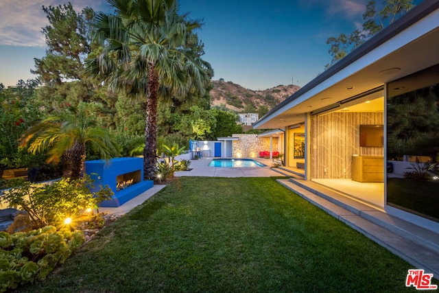 yard at dusk featuring a fenced in pool, a fireplace, a mountain view, and a patio