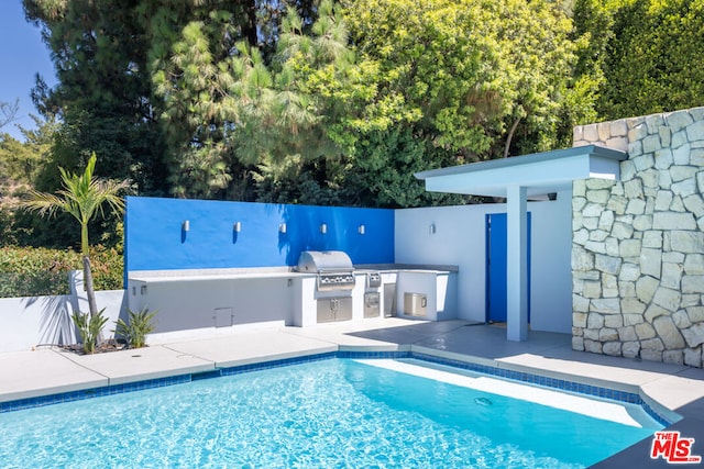 view of swimming pool featuring an outdoor kitchen, grilling area, and a patio area