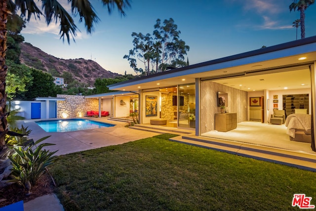 pool at dusk featuring a storage shed, a mountain view, a patio area, and a lawn