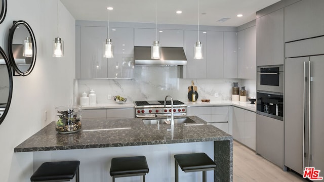 kitchen featuring a breakfast bar area, built in refrigerator, ventilation hood, hanging light fixtures, and backsplash