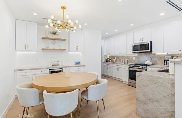 kitchen featuring sink, hanging light fixtures, stainless steel appliances, light hardwood / wood-style floors, and white cabinets