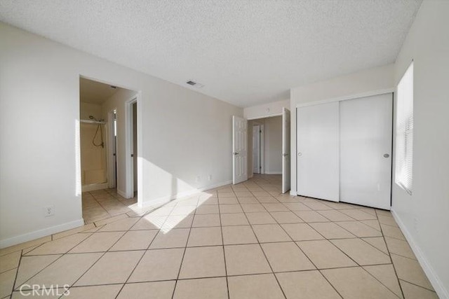 unfurnished bedroom featuring light tile patterned flooring, connected bathroom, a textured ceiling, and a closet