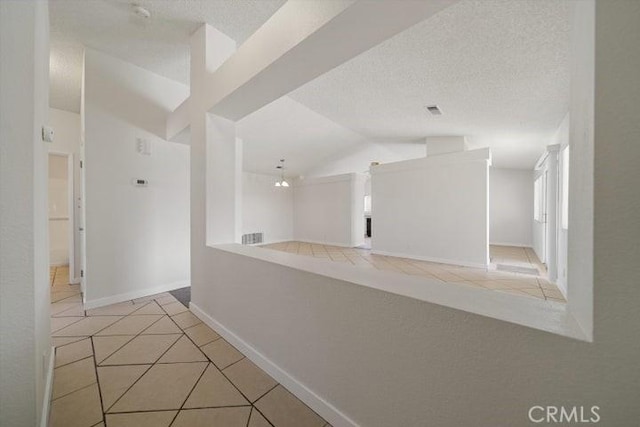 hall with lofted ceiling, a textured ceiling, and light tile patterned floors