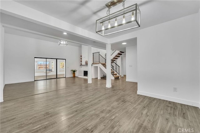 unfurnished living room featuring stairs, baseboards, and wood finished floors