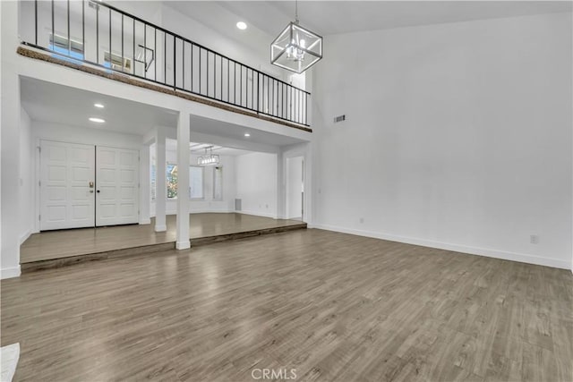 unfurnished living room with a high ceiling, wood finished floors, baseboards, and a chandelier