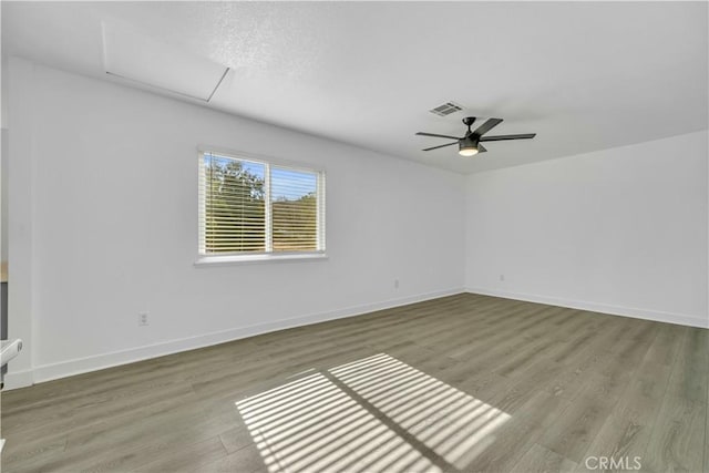 spare room featuring visible vents, attic access, baseboards, and wood finished floors