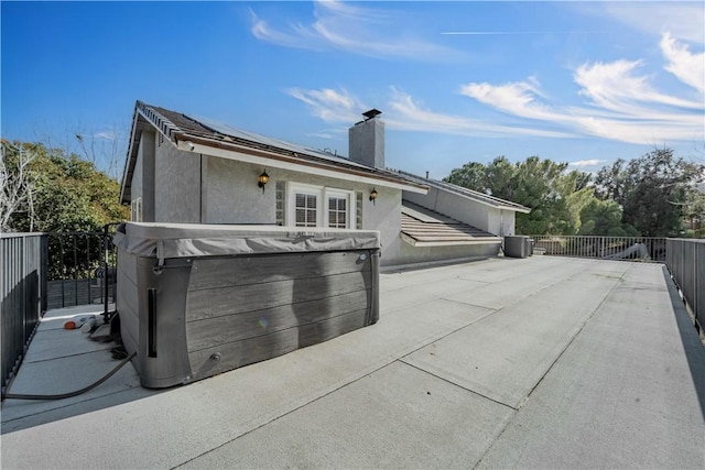 view of home's exterior featuring a patio area, fence, roof mounted solar panels, and a hot tub