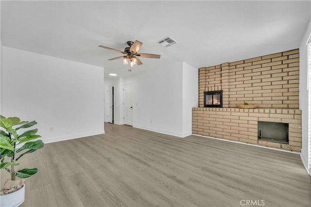 unfurnished living room featuring a ceiling fan, wood finished floors, a fireplace, and visible vents