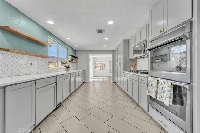 kitchen with open shelves, gray cabinetry, light countertops, and stainless steel appliances