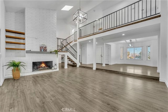 unfurnished living room featuring a notable chandelier, a brick fireplace, wood finished floors, and stairs