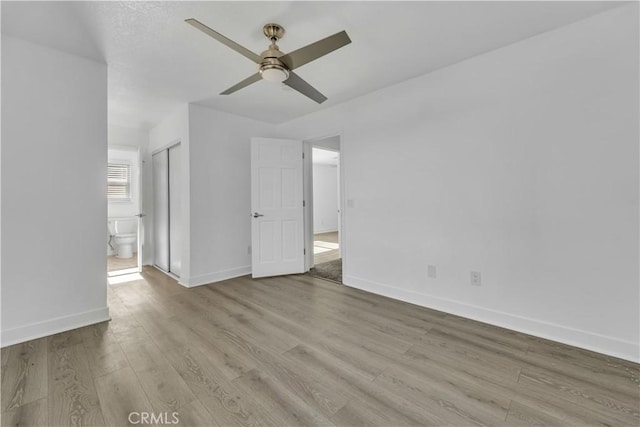 unfurnished bedroom featuring ceiling fan, connected bathroom, baseboards, and wood finished floors