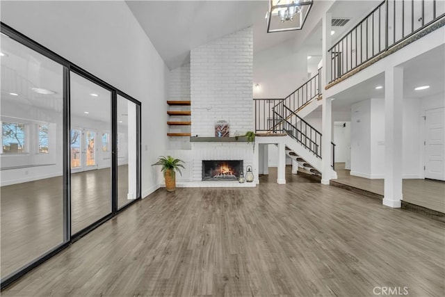 unfurnished living room featuring stairway, high vaulted ceiling, wood finished floors, and a fireplace