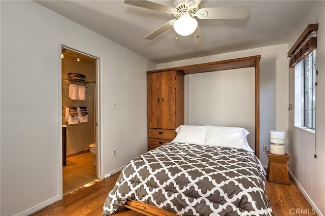 bedroom featuring baseboards, ensuite bath, wood finished floors, and a ceiling fan