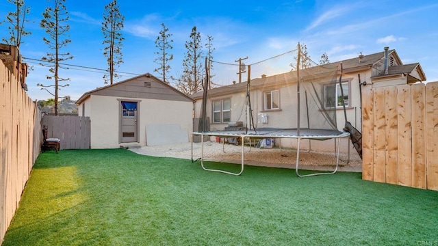 rear view of property featuring a trampoline, a lawn, and an outdoor structure