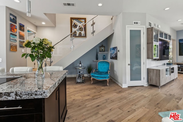 kitchen featuring dark brown cabinetry, light hardwood / wood-style flooring, and light stone countertops