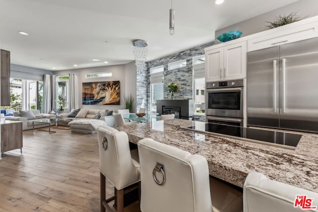 kitchen featuring light stone counters, white cabinetry, light hardwood / wood-style flooring, a kitchen breakfast bar, and stainless steel appliances